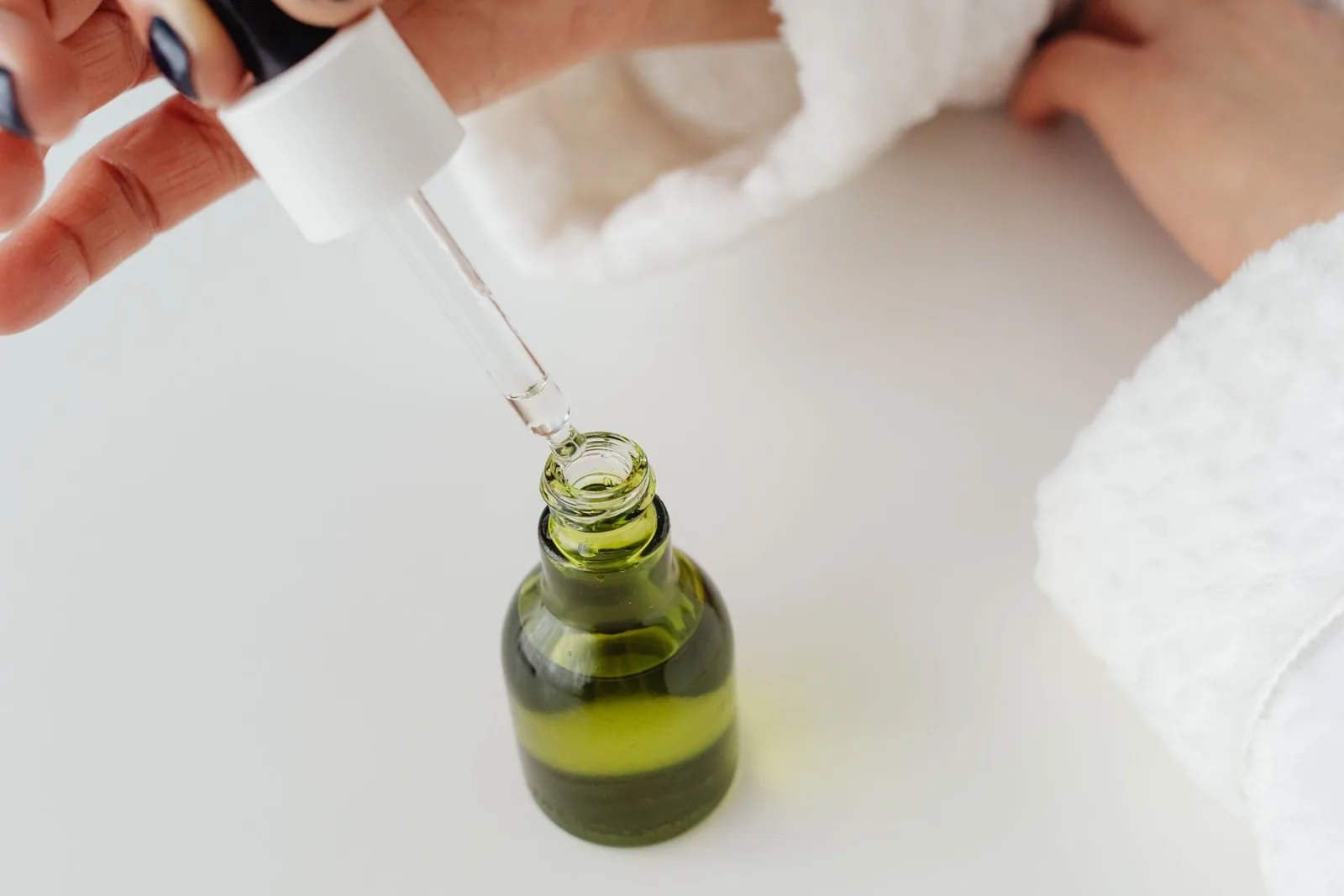 Hand holding a dropper over a green glass serum bottle