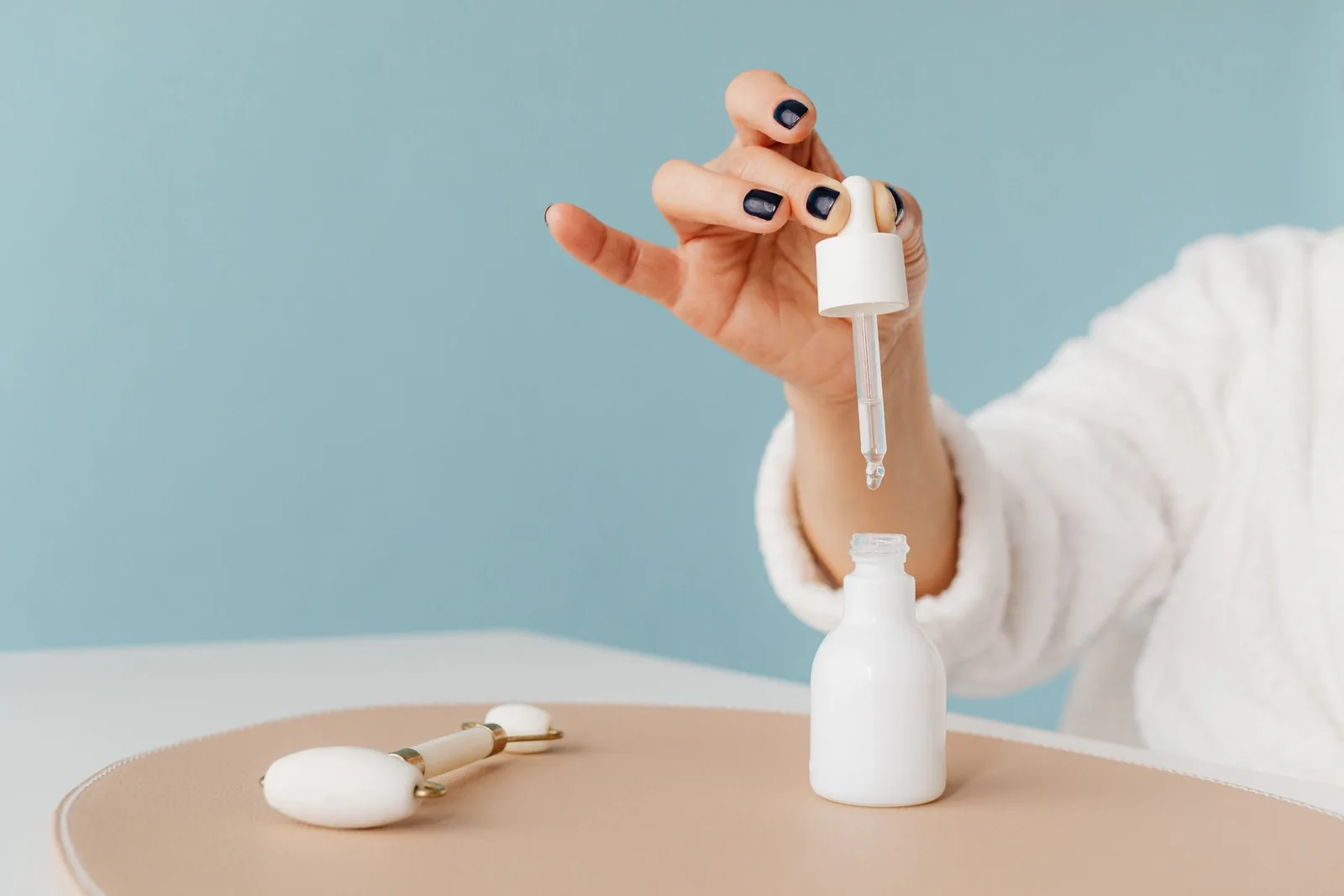 White dropper bottle and facial roller on a pastel table