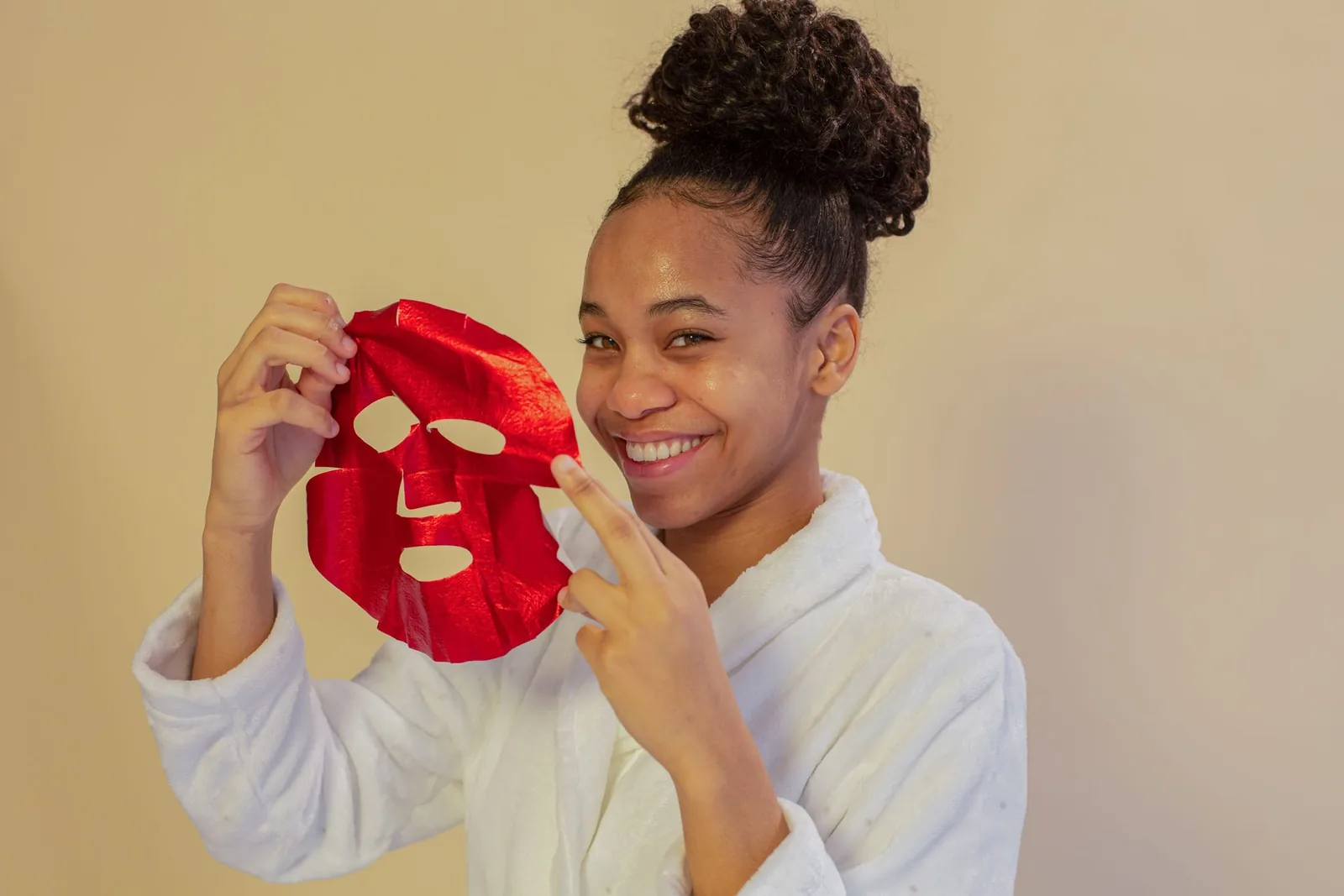 Woman in a white robe holding a red sheet mask