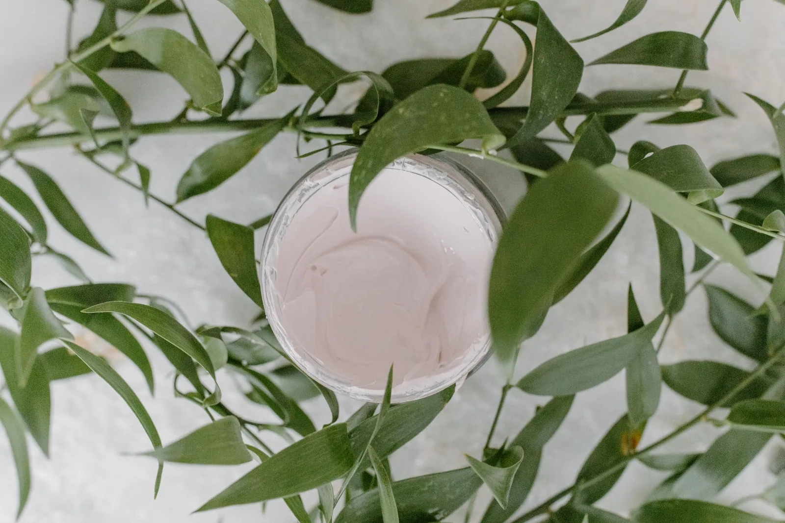 Jar of pink cream surrounded by fresh green leaves