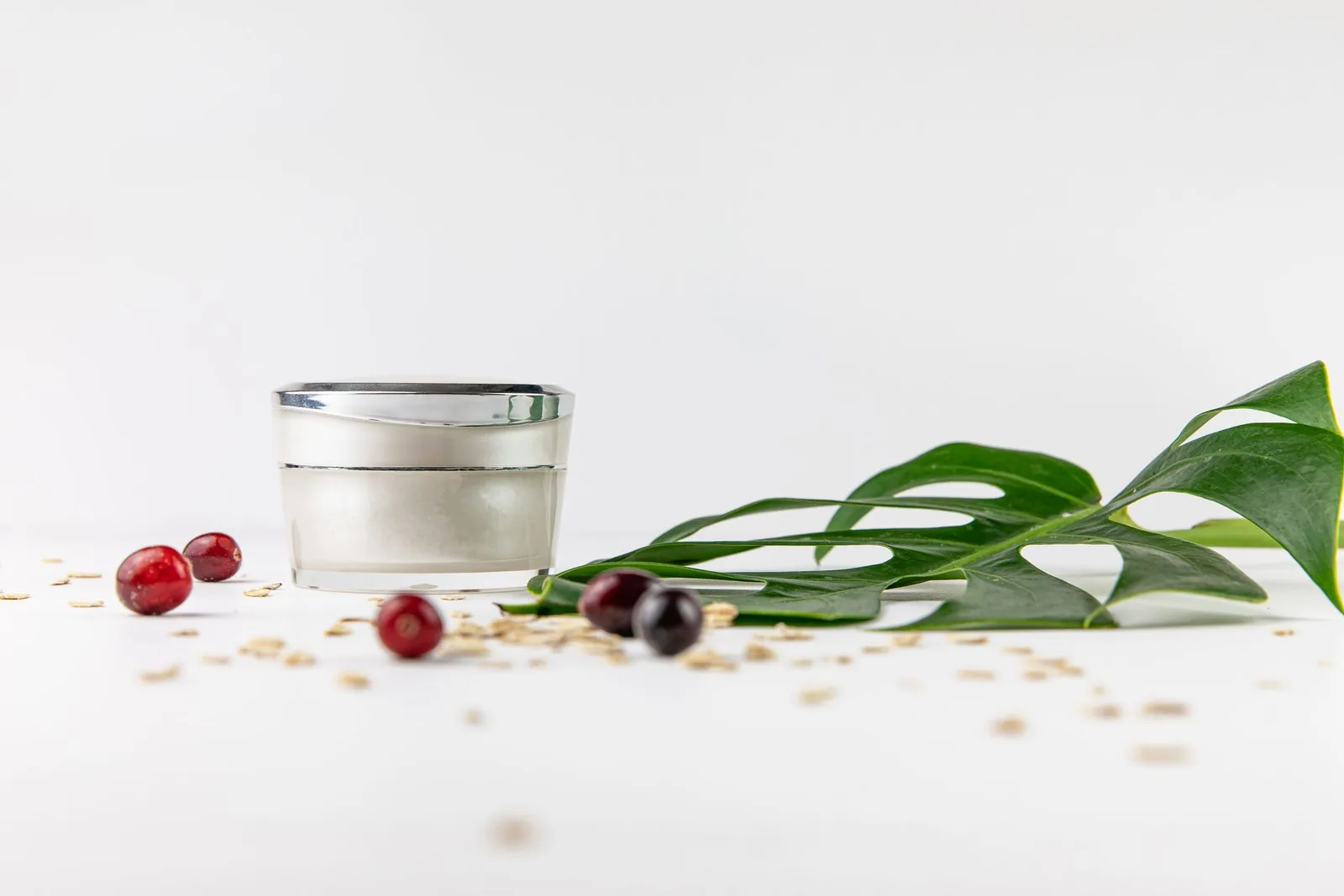 Silver cream jar beside a green leaf and red berries