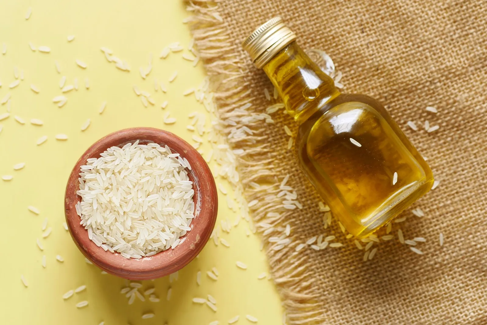 Glass bottle of oil next to a bowl of rice grains