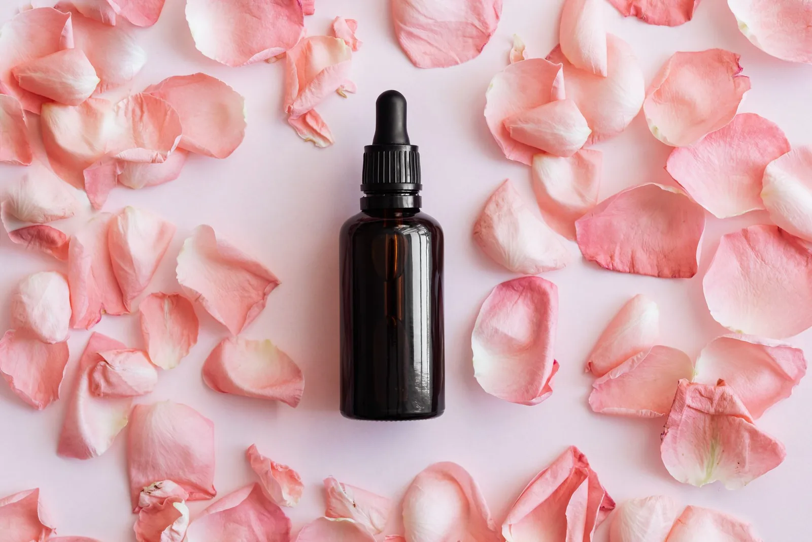 Dark glass dropper bottle lying on pink rose petals