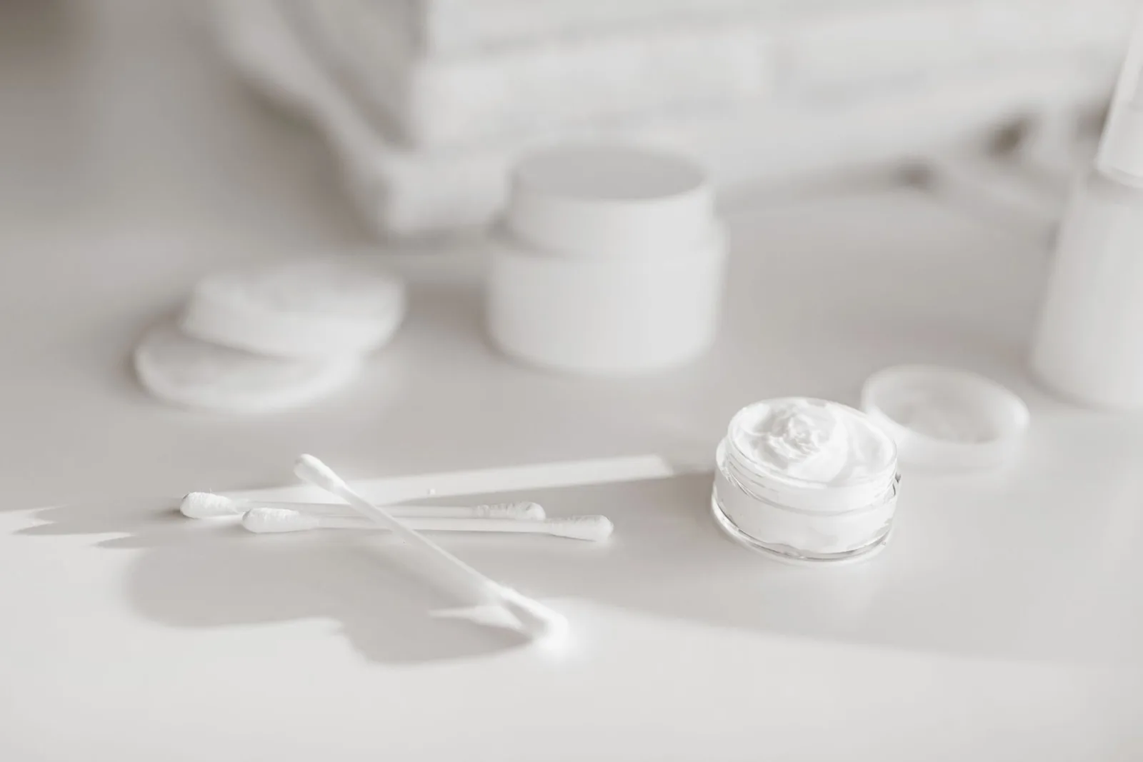 White cream jar, cotton pads and swabs on a white table