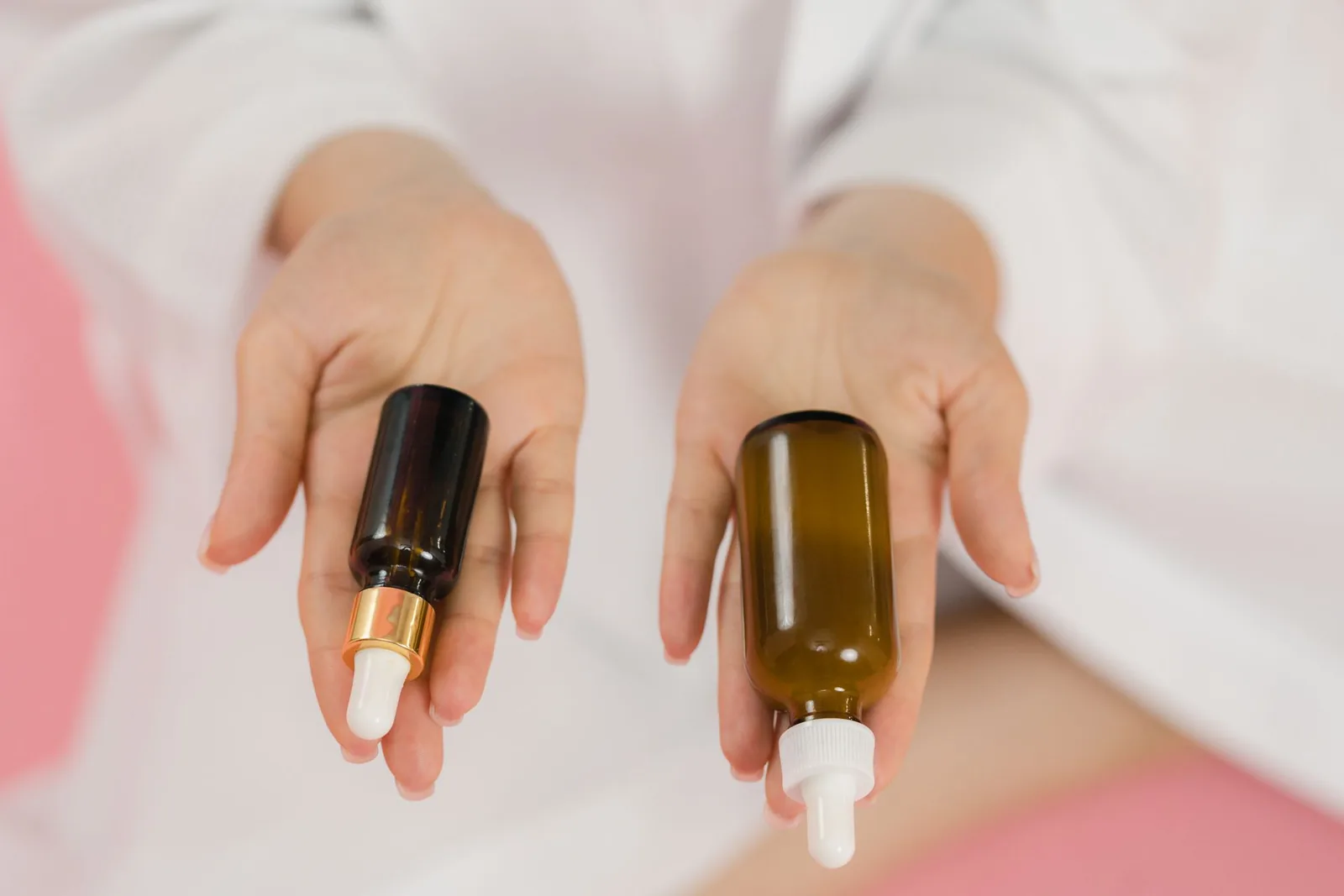 Hands holding two glass skincare bottles with droppers