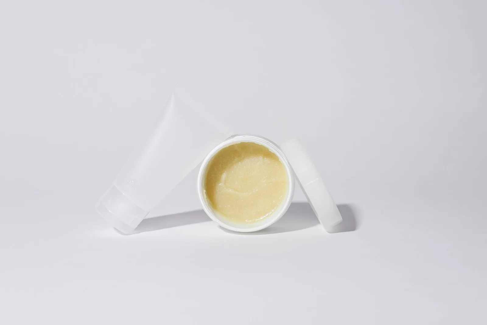 White tube and jar of yellow balm on a white background