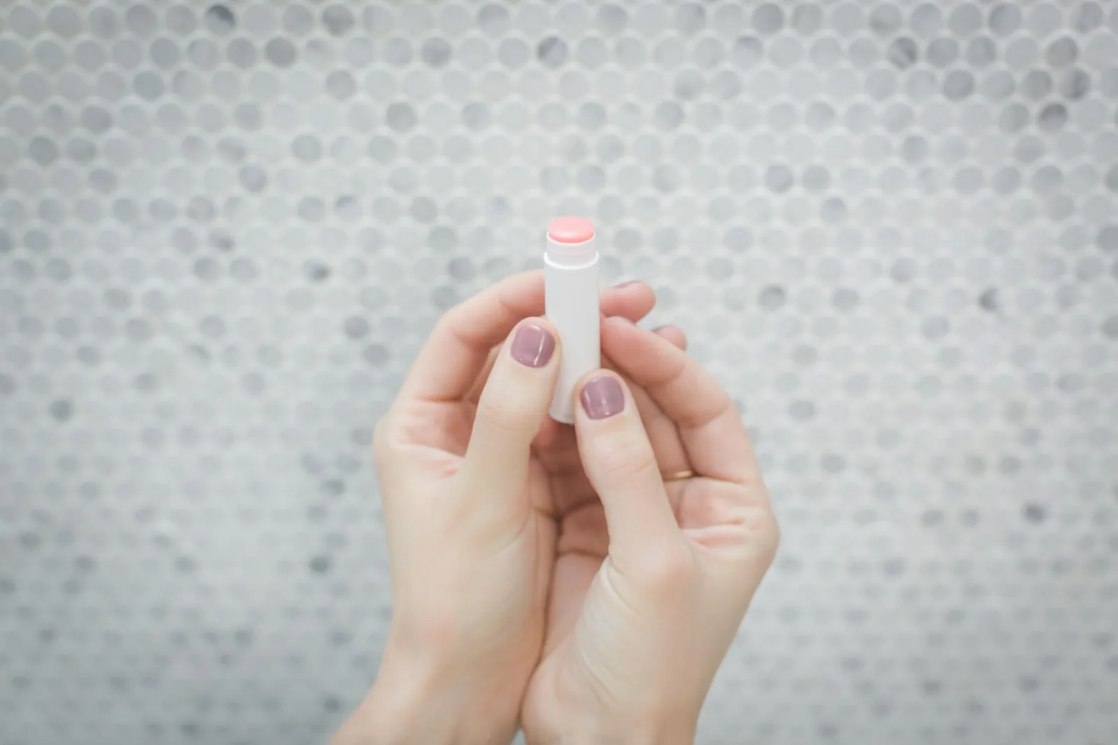 Hands holding a pale pink lip balm tube against tiles