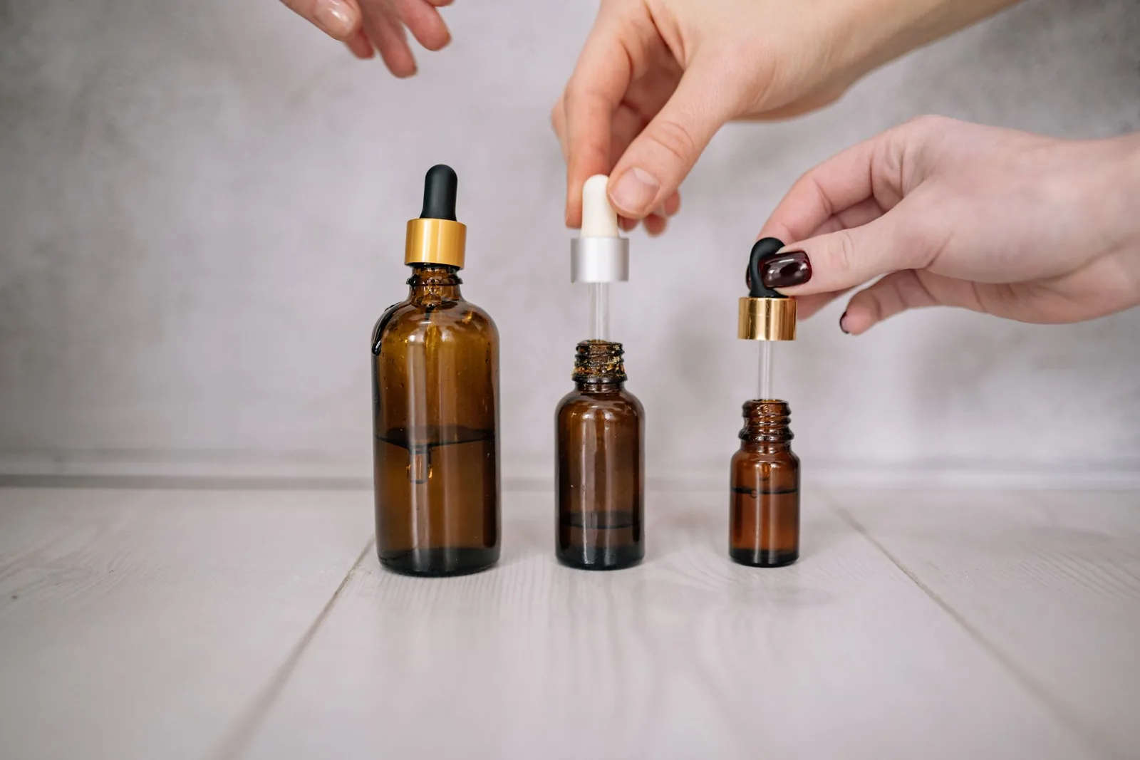 Hands holding amber glass dropper bottles over a wooden table