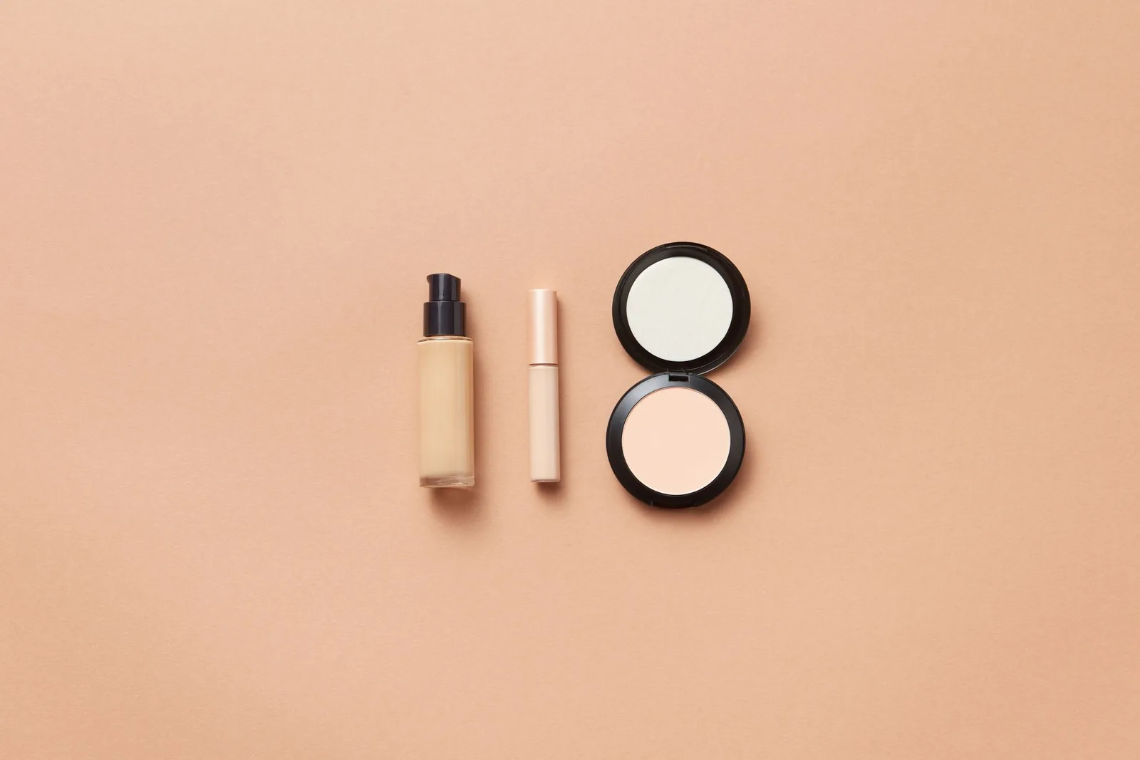 Foundation, concealer and compact powder laid out on beige background