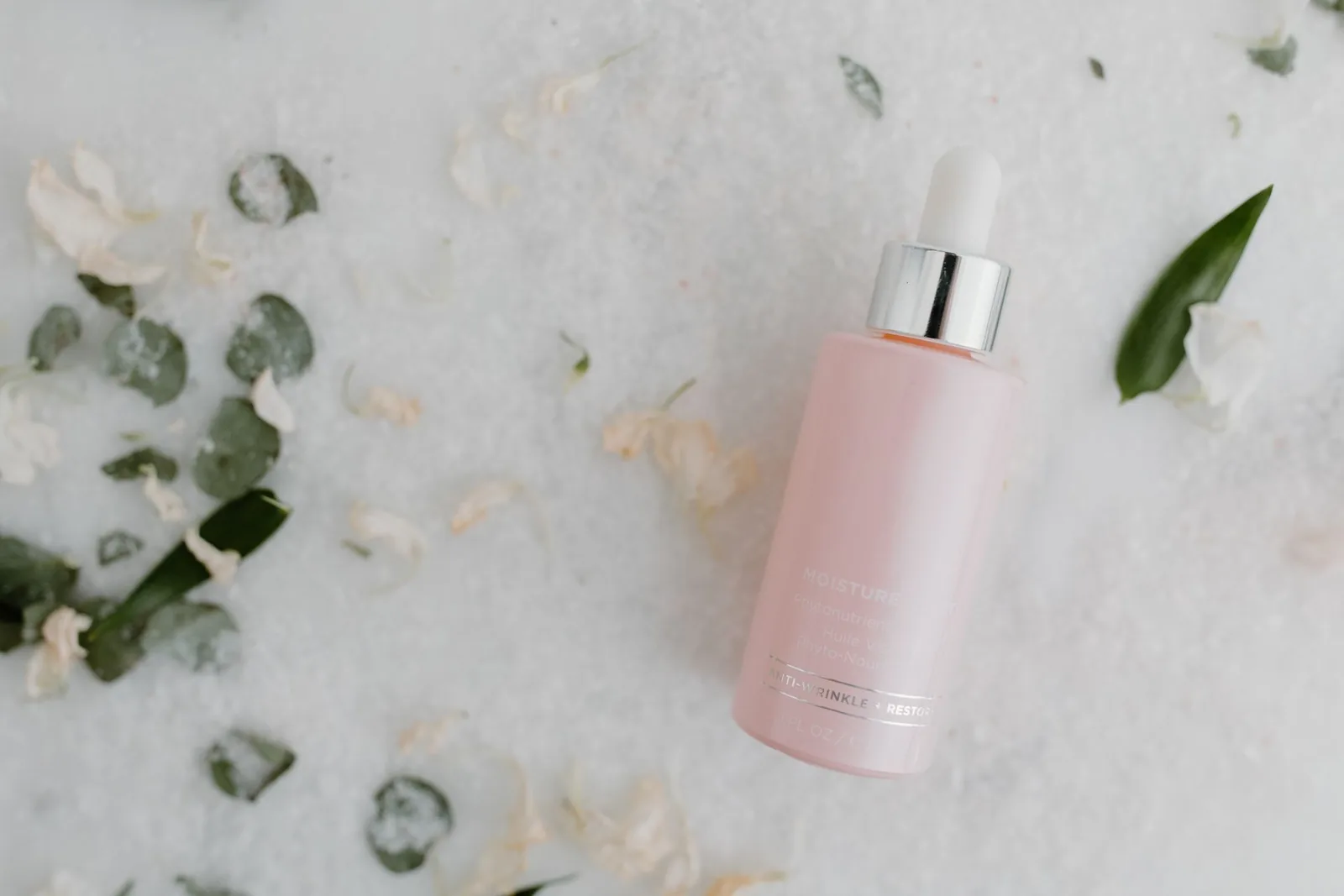 Pink glass dropper serum bottle on white salt with eucalyptus leaves