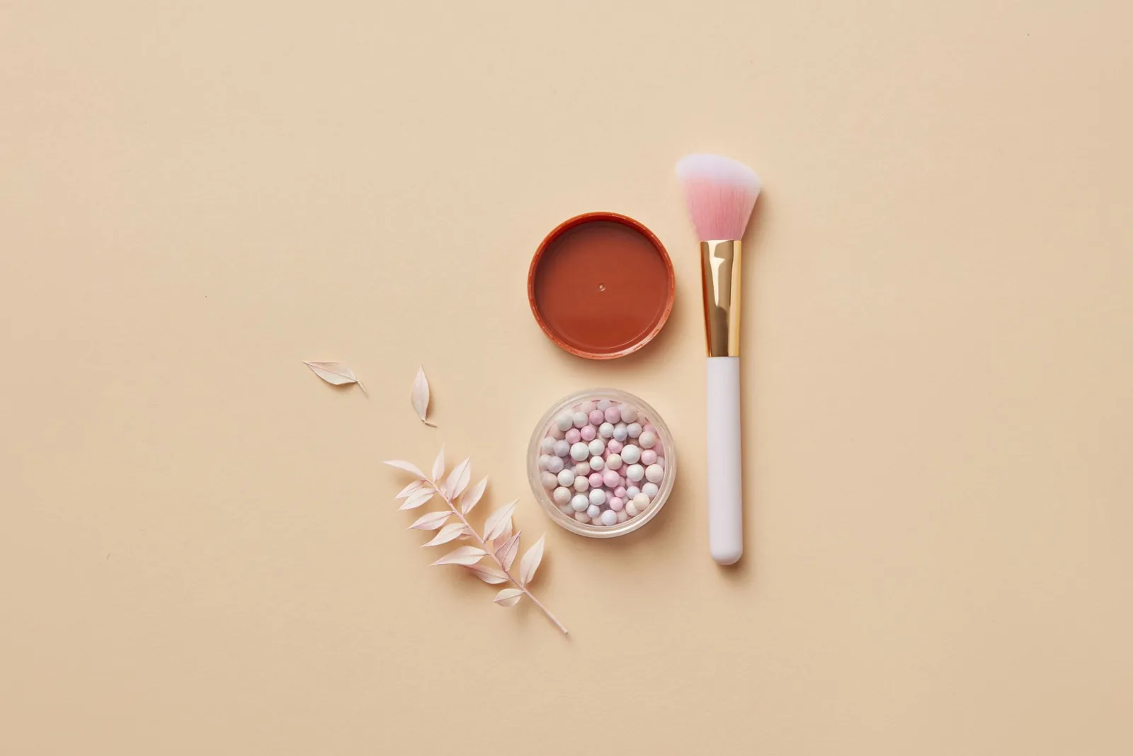 Makeup brush, blush pan and pearl powder on a peach background